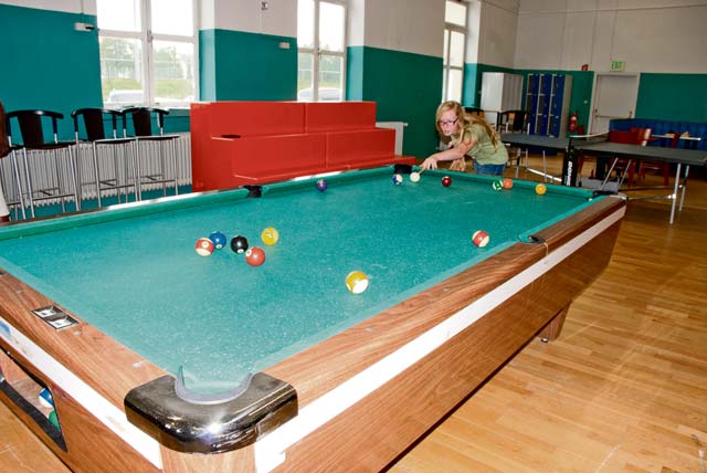 Olivia Carroll, an 11th-grade student at Patch High School, plays pool in the newly renovated high school activities room at the Patch Youth Center (the Hub). Student volunteers prepped and painted the walls and moved in new furnishings. 