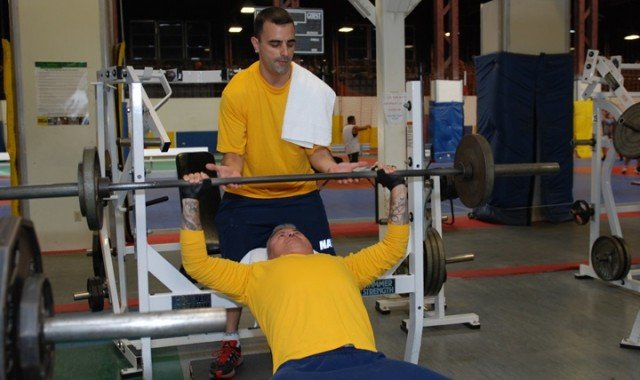 Petty Officer 1st Class Jason Pingeton, a master-at-arms, spots for Petty Officer 1st Class Humphrey Ramos, a master-at-arms, during their bench press regiment at Warehouse Gym at Naval Air Station North Island. An average of nearly 10,000 sailors do their exercise routines at the gym every month.