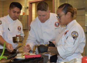 Group of chefs hover over sauce pans